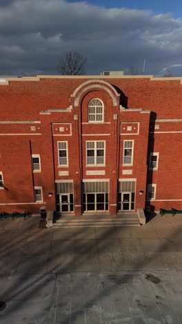 suburban brick school under bright sky showing entry path, facade, and windows in sunlight, vertical aerial orbit
