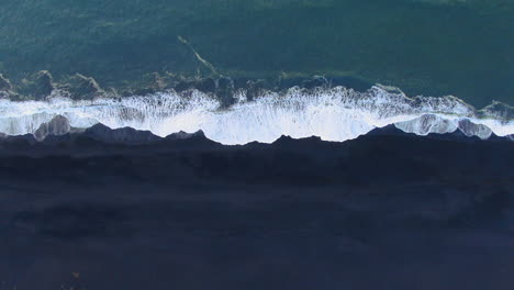 Slow-motion-drone-view-of-waves-gently-crashing-to-the-shore-amidst-an-overcast-sky-in-Iceland