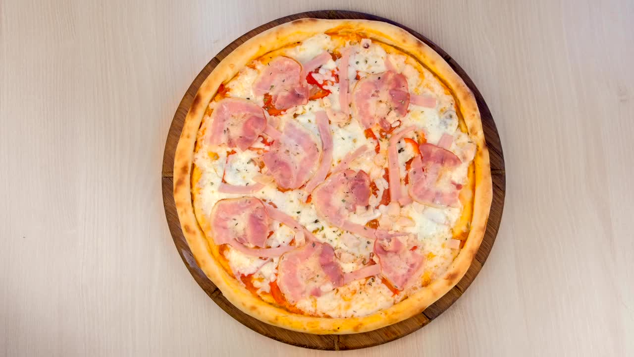 베이컨과 치즈로 된 피자는 테이블 위의 나무판 위에 있습니다.