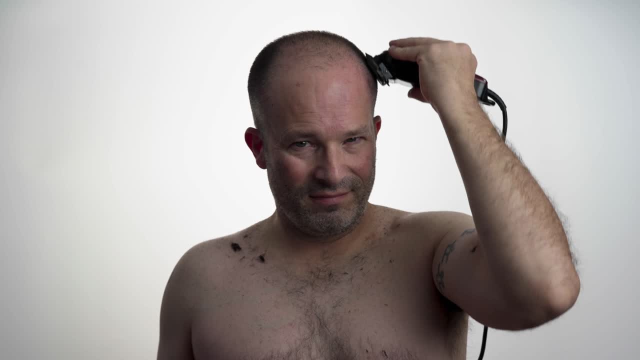 Man facing camera while he uses clippers to cut his own hair