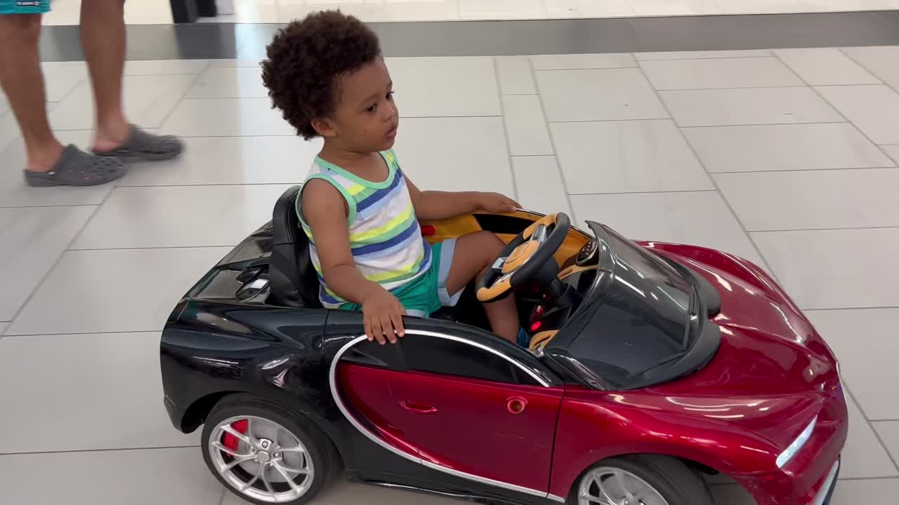 Un adorabile ed esotico bambino di due anni che si diverte a guidare un'auto giocattolo telecomandata all'interno di un centro commerciale
