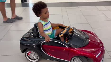 adorable and exotic two year old child enjoying riding a remote controlled toy car inside a mall