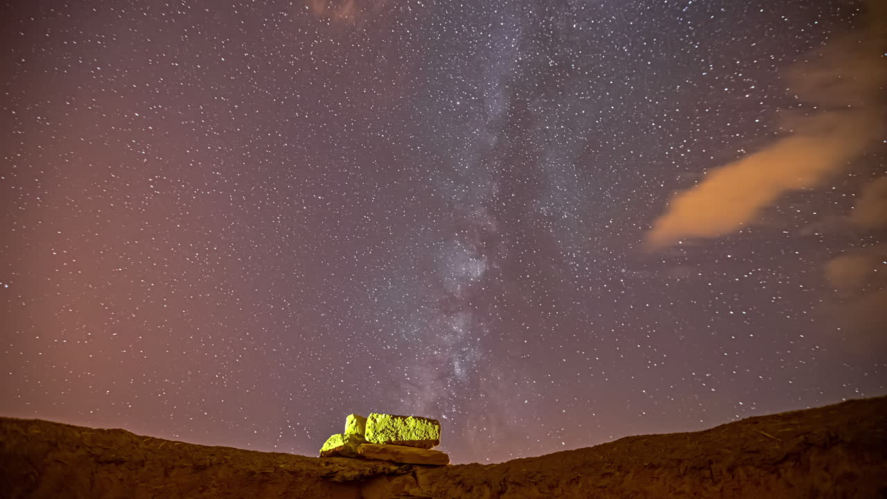 Time Lapse Of Starry Night Time Sky With Orange Rolling Clouds Above Rock Resting On Edge