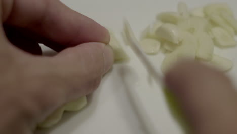 Schließen-Sie-Herauf-Hand,-Die-Knoblauch-Mit-Kleinem-Küchenmesser-Auf-Schneidebrett-Schneidet