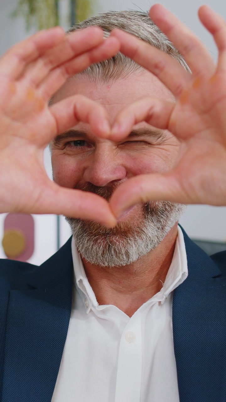 Zralý podnikatel vytváří symbol lásky, ukazuje znamení srdce do kamery, vyjadřuje romantické pocity