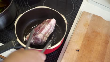 vista de arriba hacia abajo de la panza de cerdo enrollada que se coloca en una sartén caliente humeante con pinzas