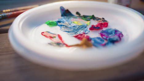 close up of artist hand pouring bright blue paint from jar onto plate, vibrant hues mixing on textured surface, morning sunlight glinting on matte acrylic, focus on fluid color movement