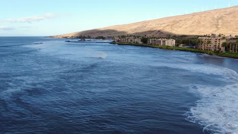 flying over maalaea ocean harbor with windmills on the west maui mountain range and waves