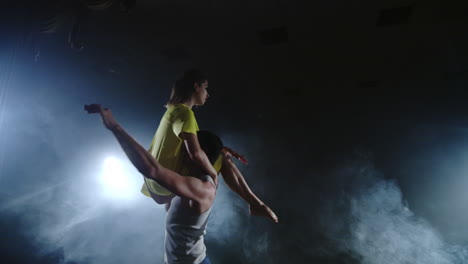 a young man is holding a woman in yellow dress holding twirling in slow motion on stage in smoke and spotlights