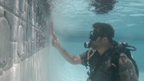 una piscina limpiada por un hombre que usa equipo de buceo mientras está bajo el agua usando un cepillo