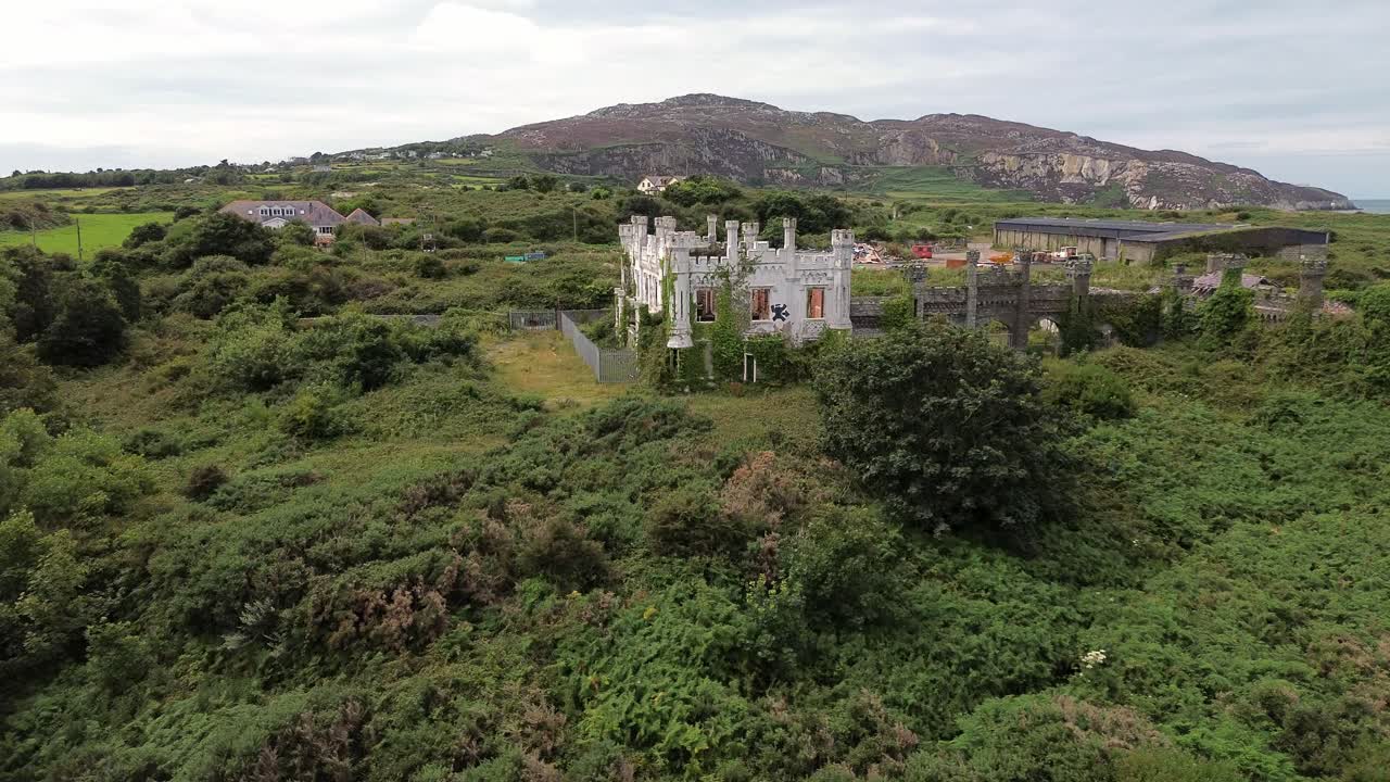 Uninhabited mental health hospital remains aerial view rising up to overgrown North Wales landmark