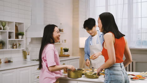부엌에서 요리하고, 말하고, 웃는 동안 세 명의 일본 친구가 팬에 재료를 붓는다