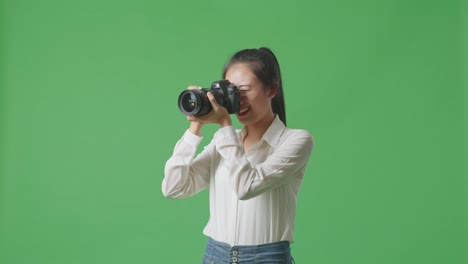 스튜디오에서 녹색 스크린 배경에 서서 사진을 찍는 카메라를 사용하는 아시아 사진작가