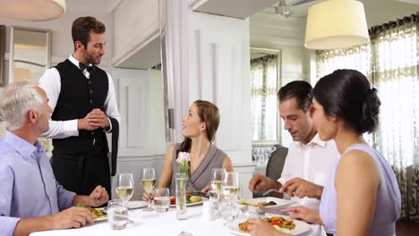 waiter attending to a table of smiling friends