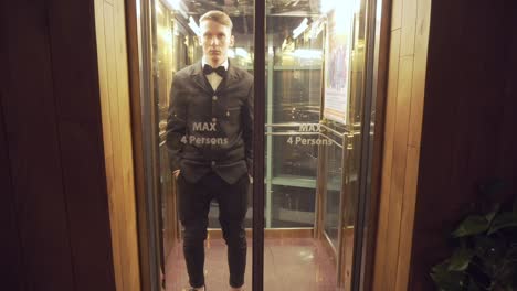 Young-and-successful-businessman-in-a-suit-with-a-bow-tie-coming-out-of-the-Elevator-with-Glass-Doors.