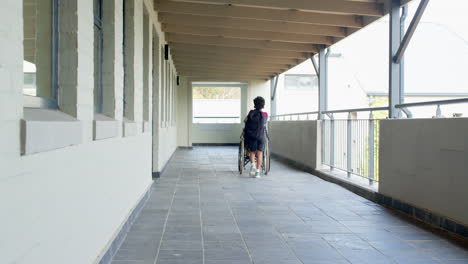 african american boy pushing wheelchair down school hallway, showing kindness and support