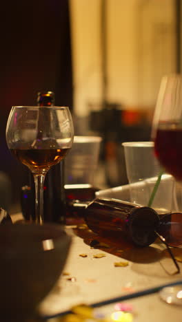 Vertical-Video-Of-Messy-Table-Covered-With-Empty-Wine-Glasses-With-Beer-Bottles-And-Snacks-After-House-Party-1