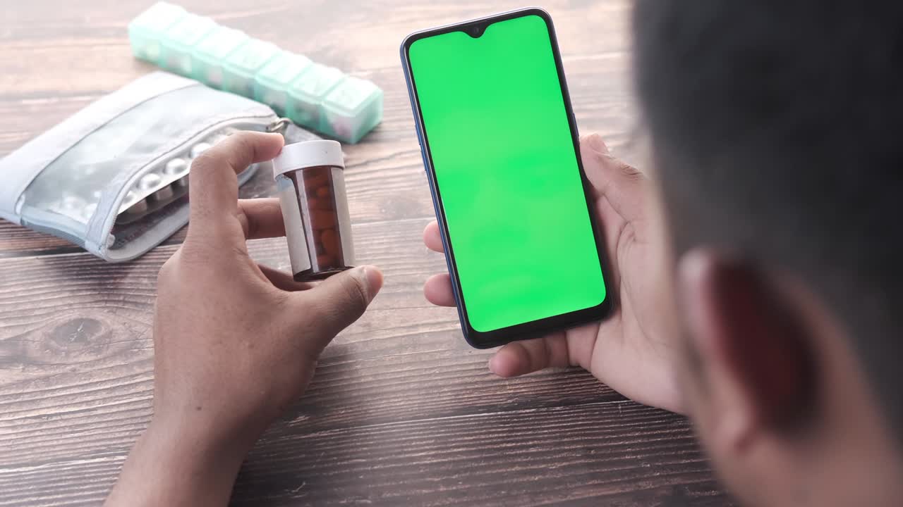 vista trasera de un joven usando un teléfono inteligente y sosteniendo un contenedor de pastillas médicas