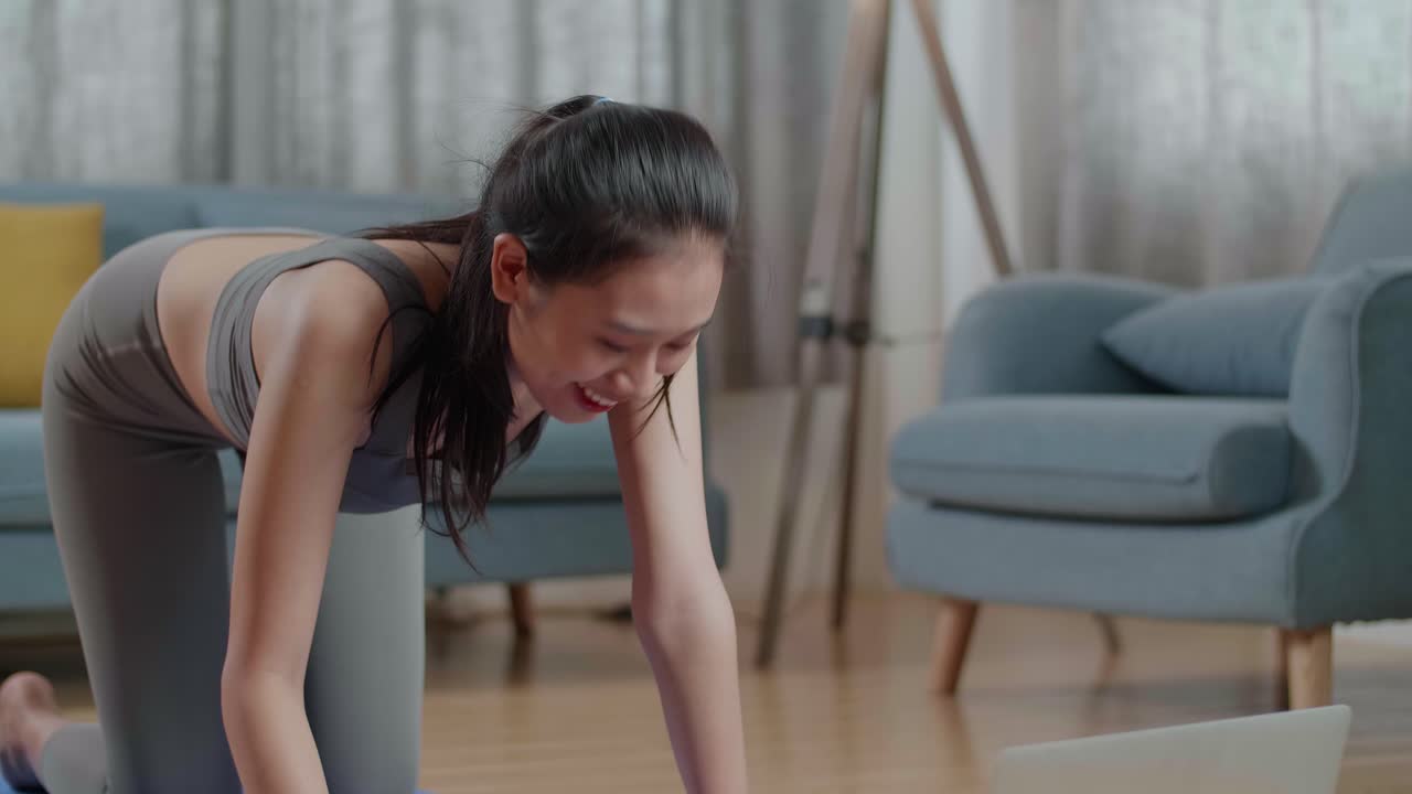 스포츠 옷을 입은 젊은 아시아 운동선수 여성이 런싱 테이블 포즈에서 요가를 하고 있습니다. 노트북 컴퓨터를 통해 온라인 코치와 함께 집에서 매트에 포즈를 취합니다.
