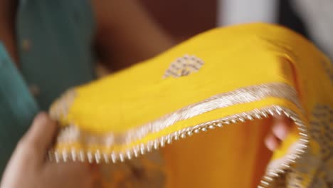 young south asian woman folding yellow indian shawl, dupatta