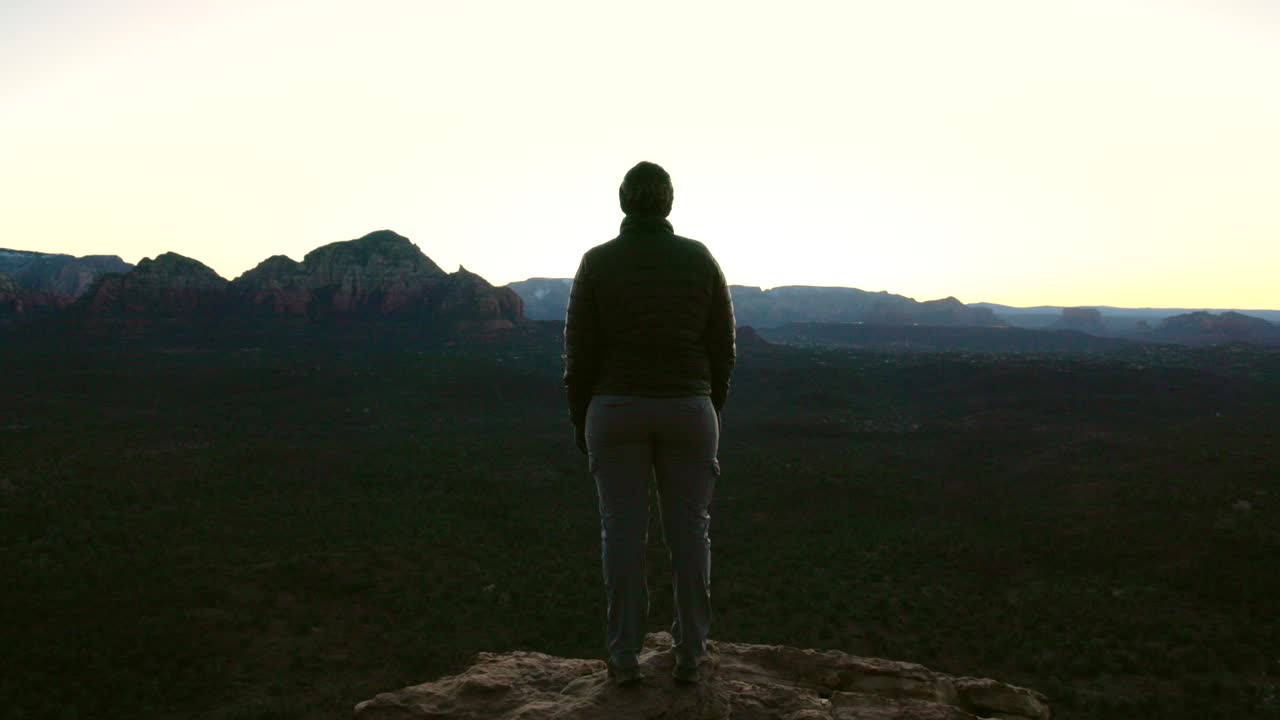 Escursionista donna cammina verso una sporgenza prima dell'alba guardando verso la valle di Sedona