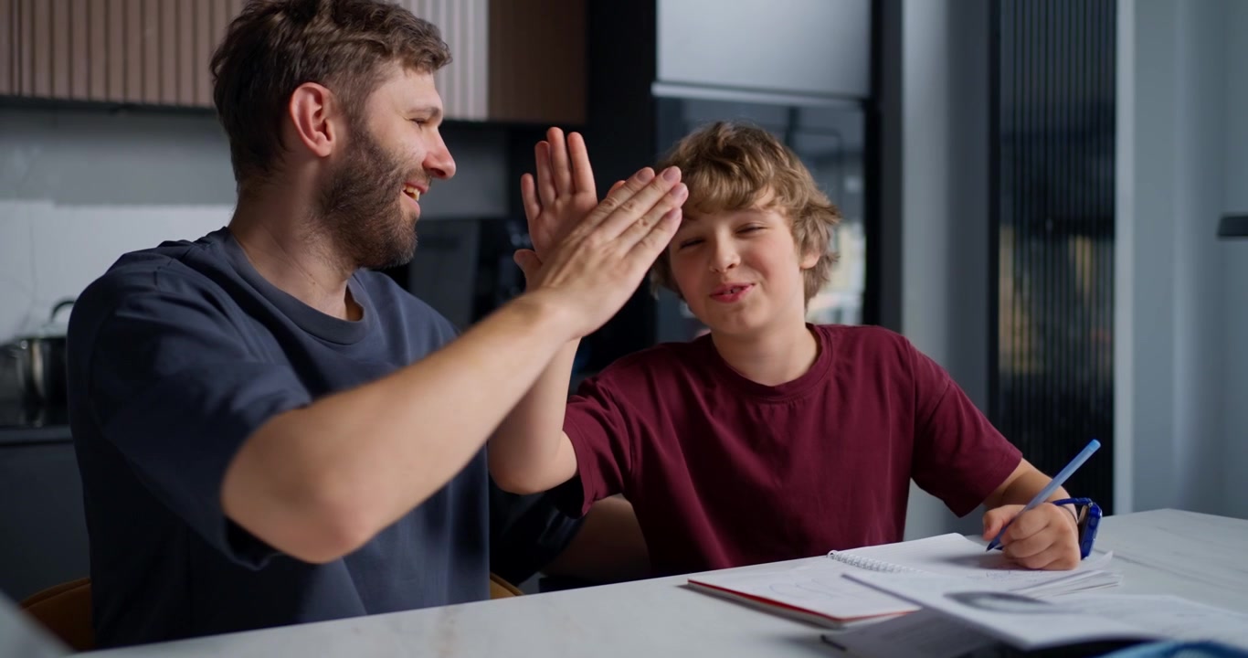 Padre e figlio che fanno i compiti insieme, si danno il cinque e ridono.