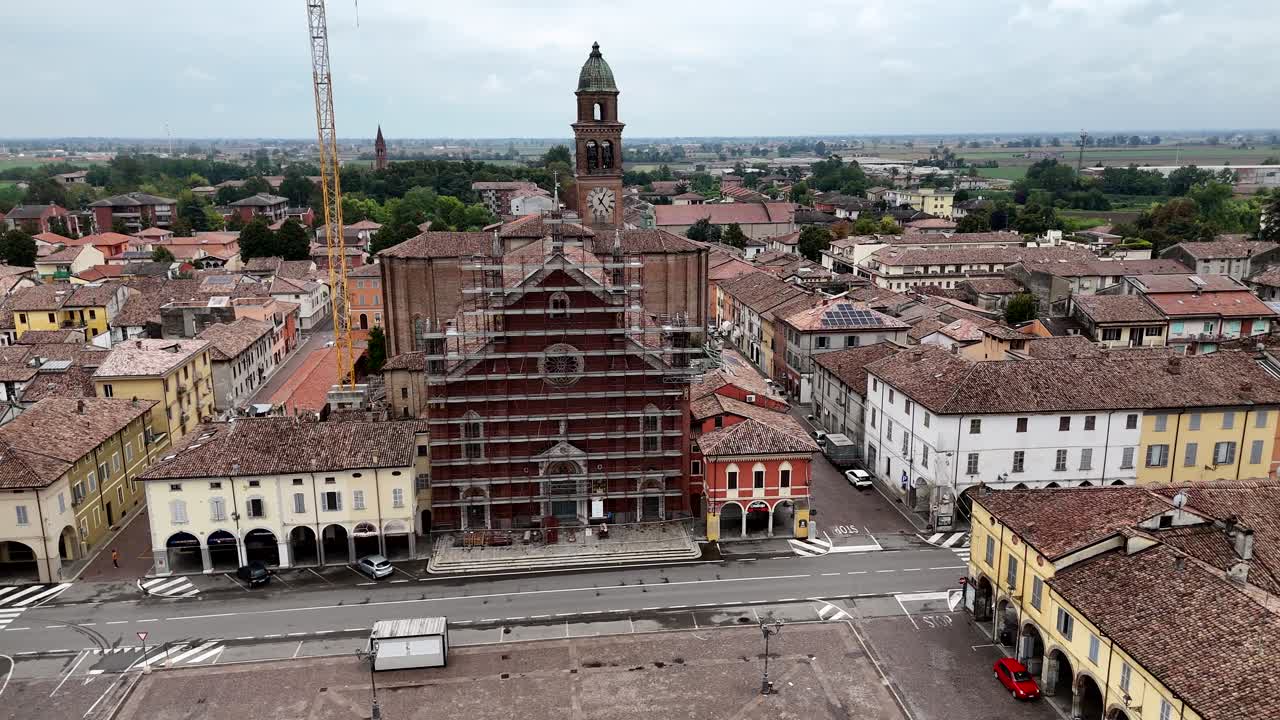 Aerial shot of the Basilica of Santa Maria delle Grazie in Cortemaggiore, Piacenza province, Italy, with scaffolding on the façade during restoration works, surrounded by arcaded buildings and square