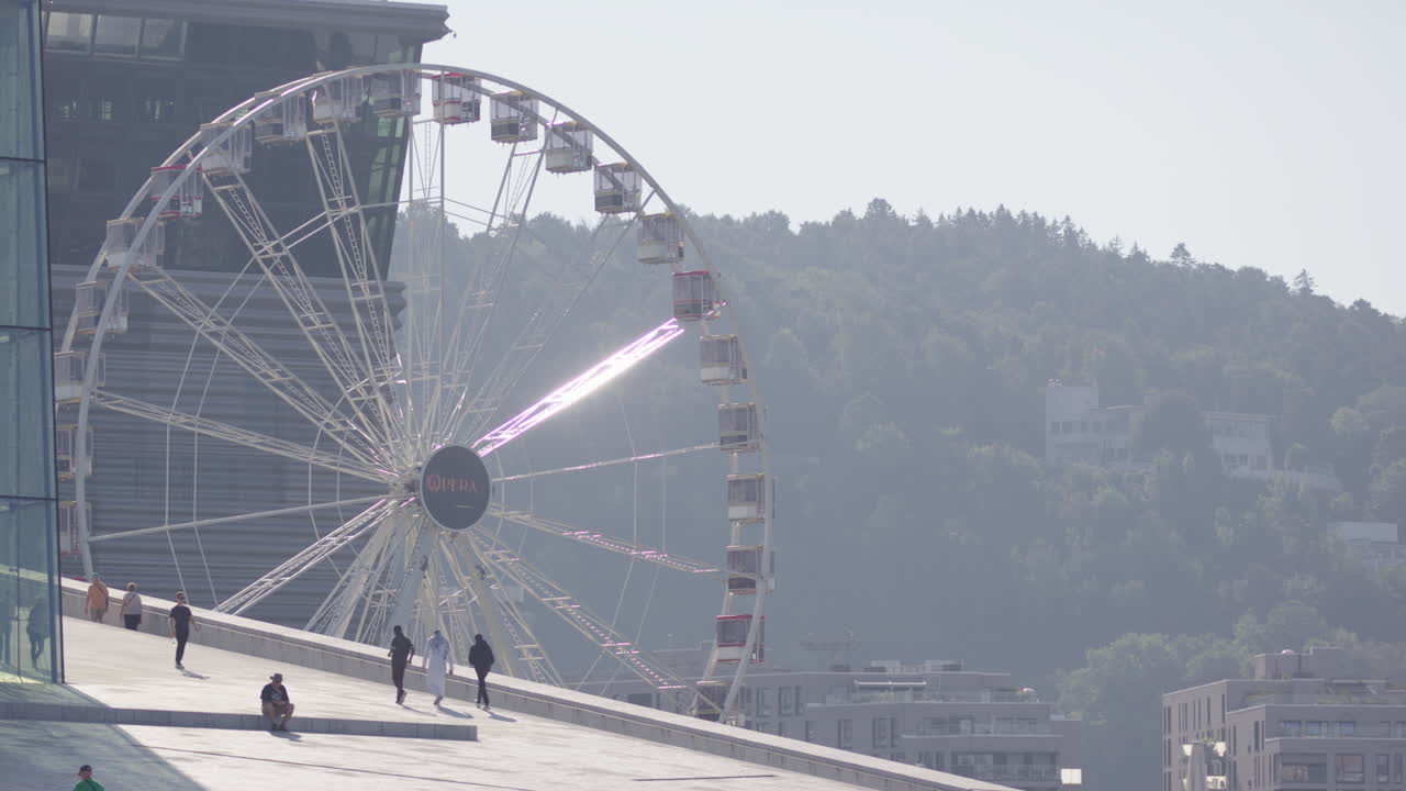 People stroll on sloped roof of Oslo Opera House with view of Opera Ferris Wheel