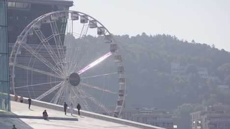 people stroll on sloped roof of oslo opera house with view of opera ferris wheel