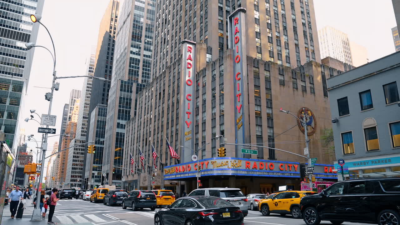 New York, USA, 1 August 2025: Flow of cars move by the street of New York, USA. Low angle view at the building of Radio City Hall in Manhattan