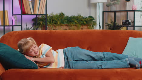 tired school girl child kid lying down in bed taking a rest at home, napping, falling asleep on sofa