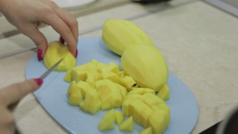 mujer cortando patatas en la tabla de cortar azul