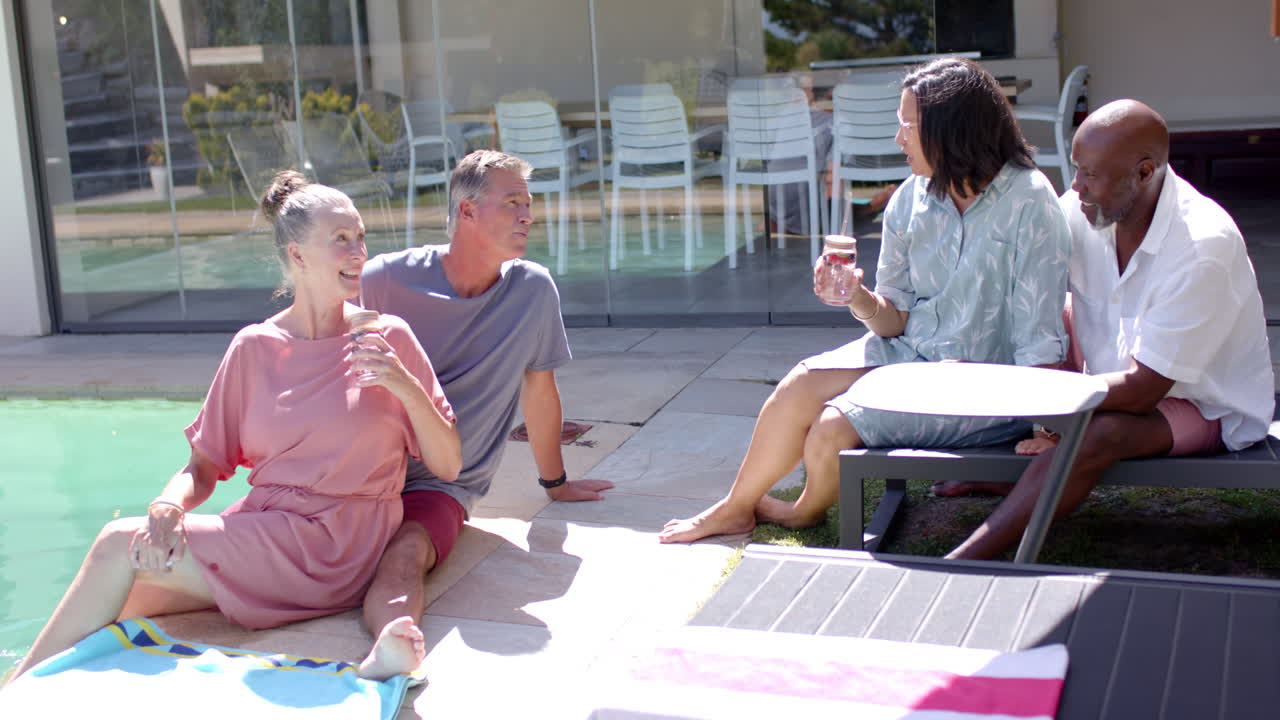 By pool, diverse senior friends relaxing with drinks, sharing joyful moments under sunshine