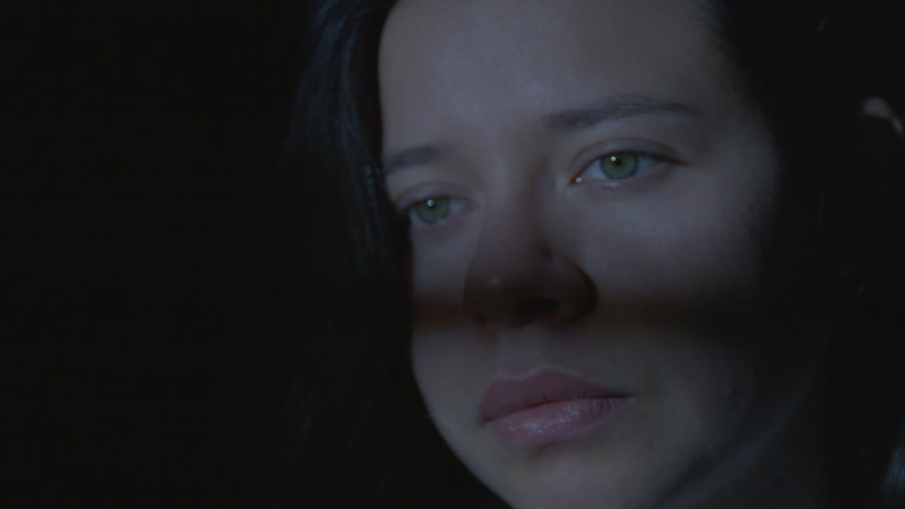 Intimate close-up shot of a young Latina girl gazing pensively, with wind softly tousling her hair. Dim lighting creates a moody, contemplative atmosphere, capturing serene introspection