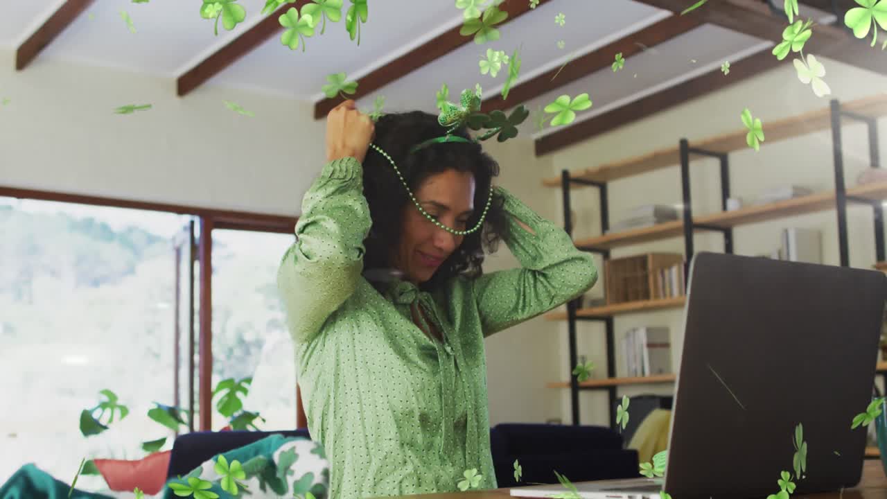 Animation of shamrocks falling and biracial woman in shamrock glasses celebrating st patrick's day