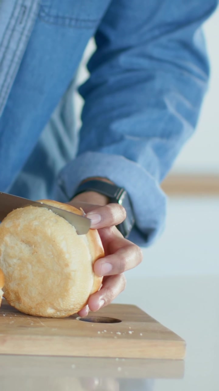 Vertical video: Entering man's hands in denim grabbing knife sawing bun at home near bowl to eat