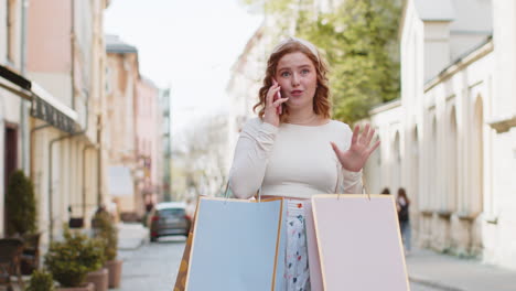 Mujer-Feliz,-Consumidora-Adicta-A-Las-Compras-Después-De-Hacer-Compras-En-Rebajas-Con-Bolsas-Llenas-De-Regalos-Hablando-Por-Teléfono-Inteligente