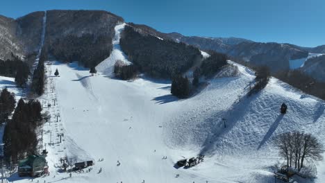 pull away and orbiting shot of bottom of ski run, skiers arriving at base of mountain lining up for the chairlifts