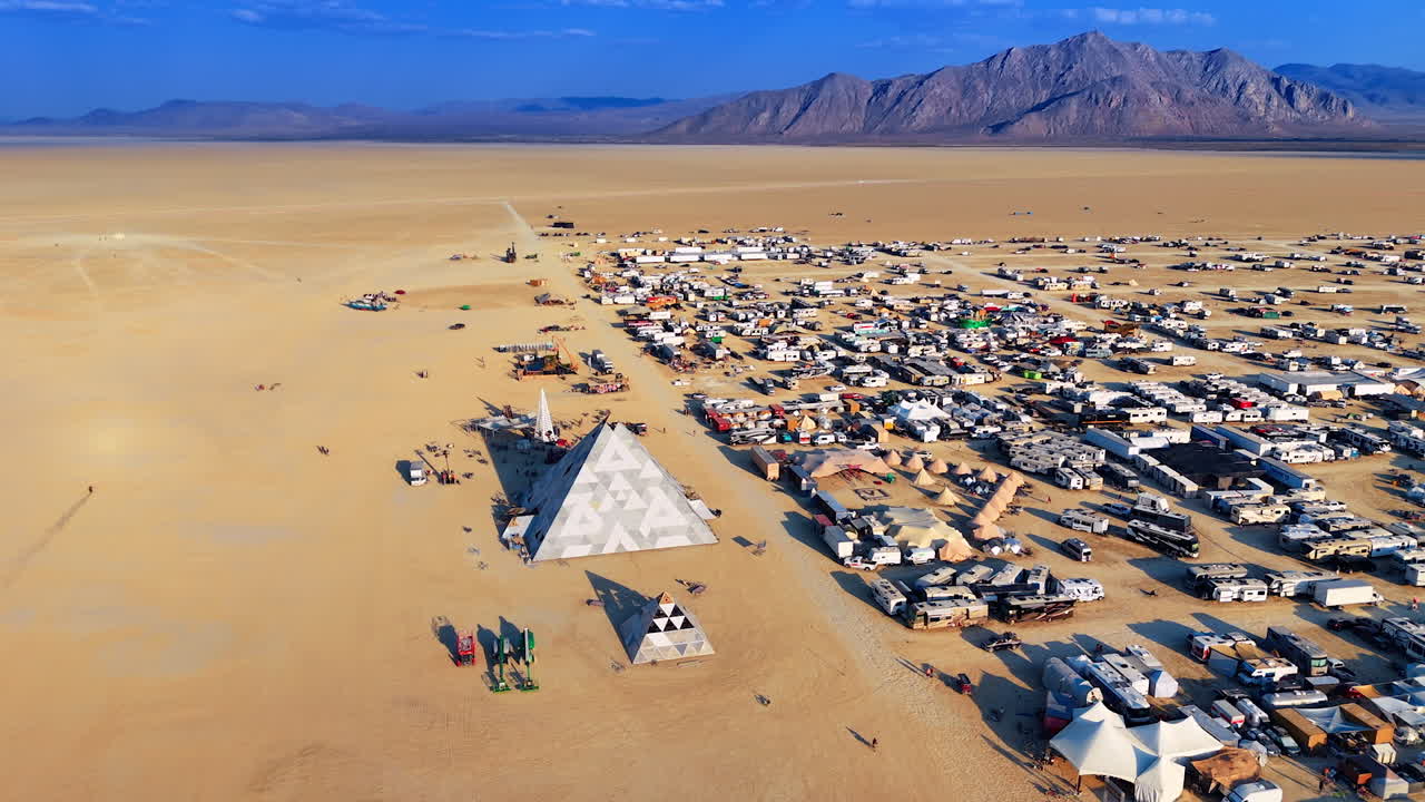 Nevada, USA, 25 August 2025: Drone panoramic view of the Burning Man camp with mirrored pyramids, tents, and vehicles surrounded by desert mountains