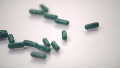 slow motion macro of green pills dropped onto white background