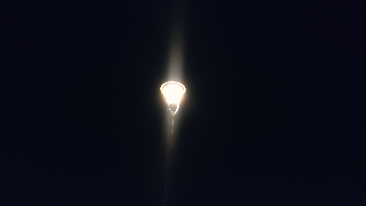 Farola solitaria brillando en la oscuridad, escena nocturna minimalista con atmósfera melancólica. Ideal para soledad, aislamiento, misterio, noche urbana, fondo cinematográfico y narración emocional.