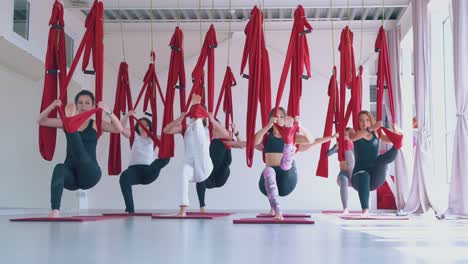 relaxed women group practices modern pilates with hammocks