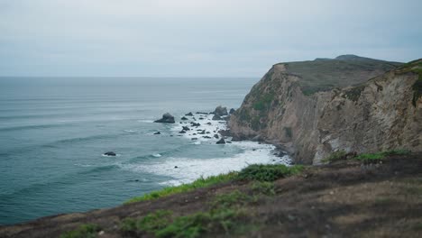 waves crashing into a steep cliff in northern california on a gloomy day