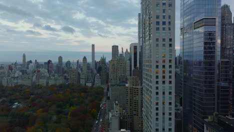 Slide-and-pan-shot-of-high-rise-downtown-buildings-and-busy-long-street-leading-about-Central-park.-Modern-skyscrapers-reflecting-twilight-sky.-Manhattan,-New-York-City,-USA