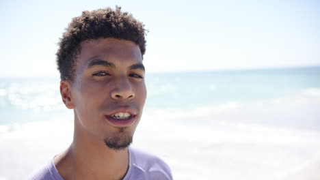 a young biracial man smiles brightly at the beach with copy space