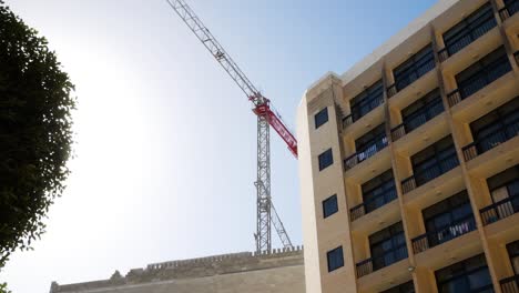 grúa torre industrial de construcción que trabaja cerca del edificio del hotel en un día ventoso en la isla de malta, vista de lapso de tiempo