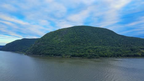 aerial drone footage descending on the hudson river in new york's hudson valley with storm king mountain in the background at sunset