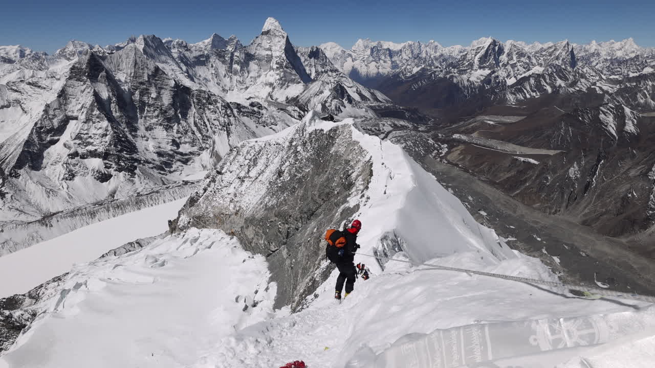 Person walking on the summit of Island Peak in Nepal with views of surrounding mountains.