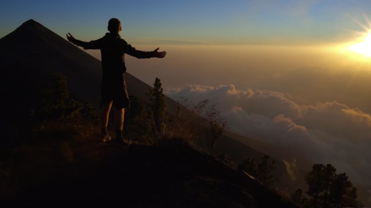 Man admiring Volcano Fuego from acatenango at sunset in Guatemala, expressing success and gratitude