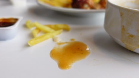 cerca de una mesa desordenada después de una comida, con salsa derramada, papas fritas, y un cuenco vacío.